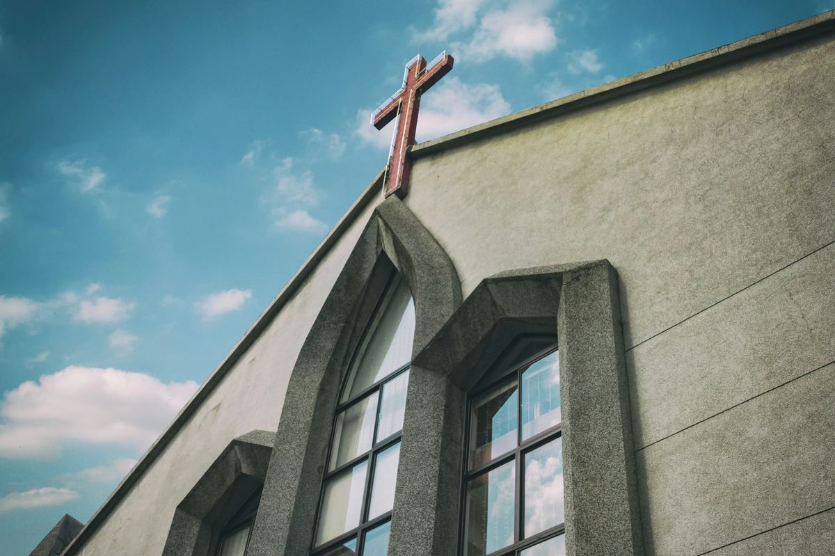 Church roofline with a cross against a bright blue sky